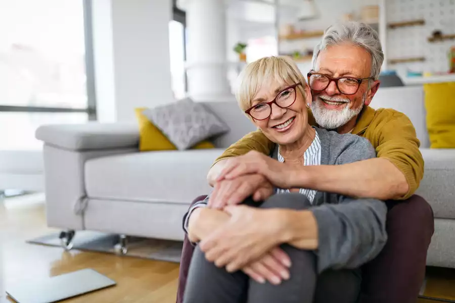 Happy senior couple smiling in each other’s embrace on the living room floor