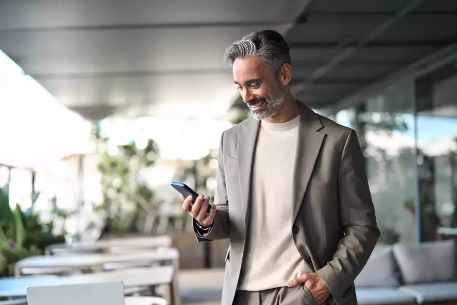 Smiling older gentleman looking down at his smartphone in a patio background setting